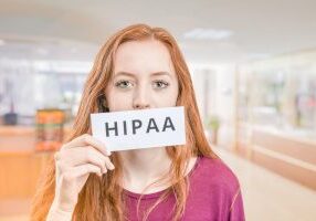 An Image of a redhead female holding a sign with the word HIPAA. Ensuring HIPAA Compliance for Healthcare